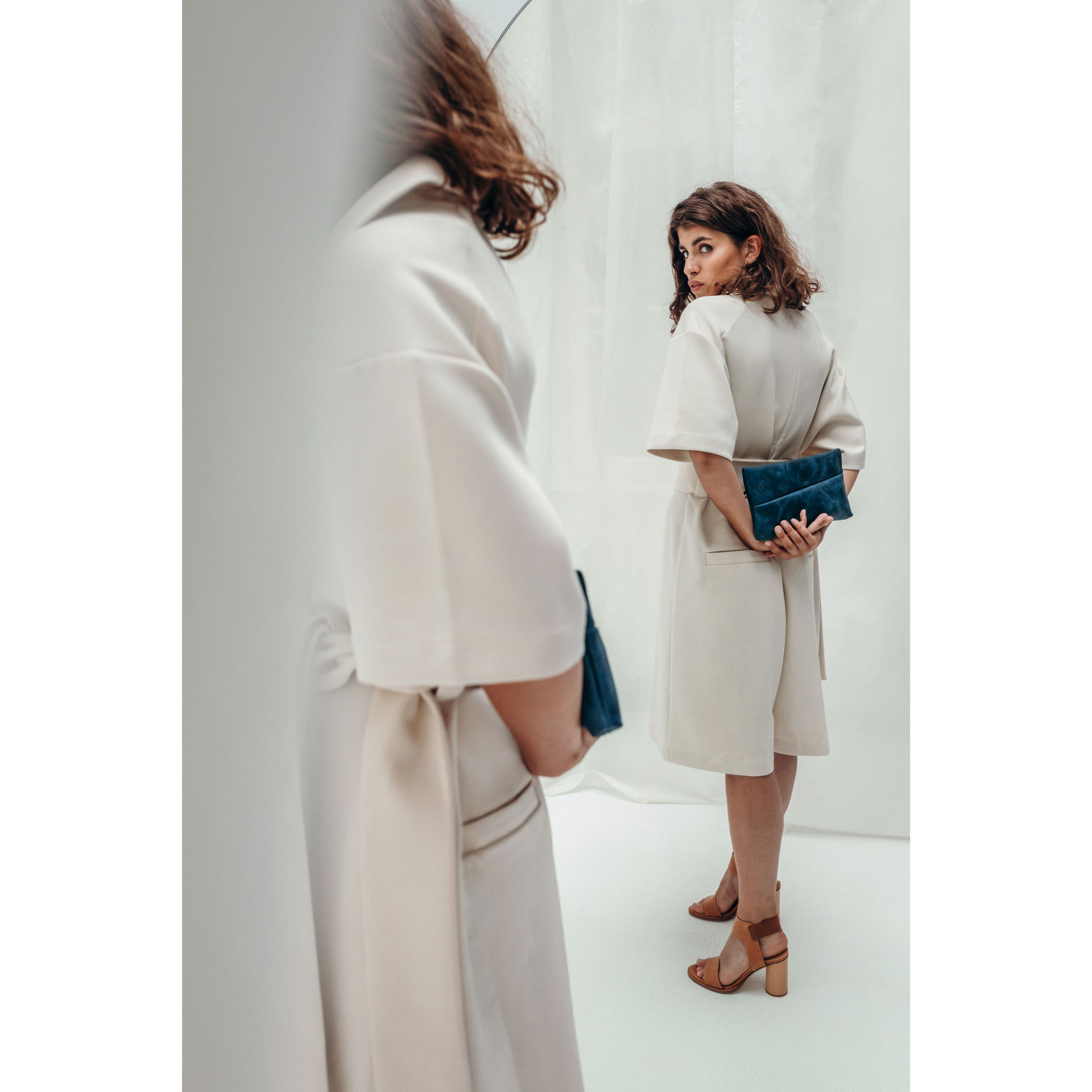 Model schaut sich im Spiegel die 3-in-1 Tasche Isa in blauem Naturleder an