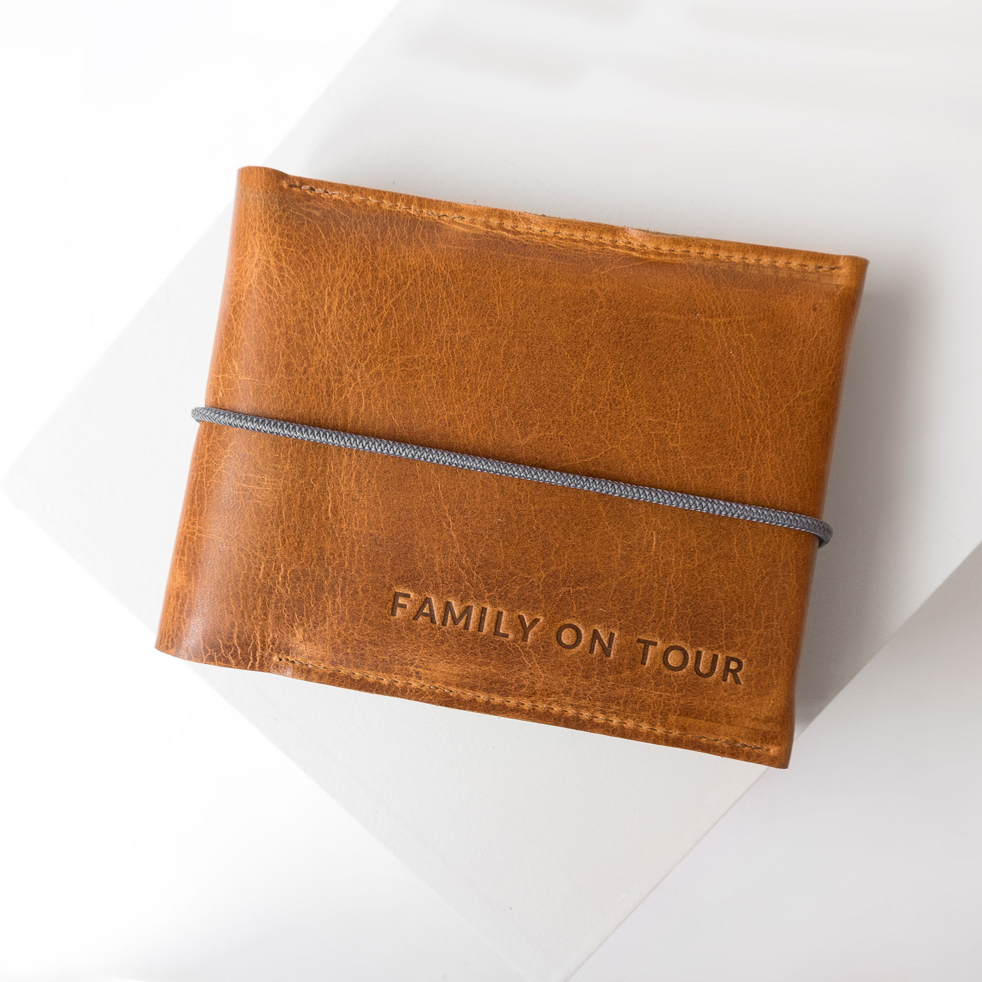 Familienreisepasshülle EVE aus nachhaltigem Naturleder in Cognac geölt mit grauem Verschlussband und individueller Prägung