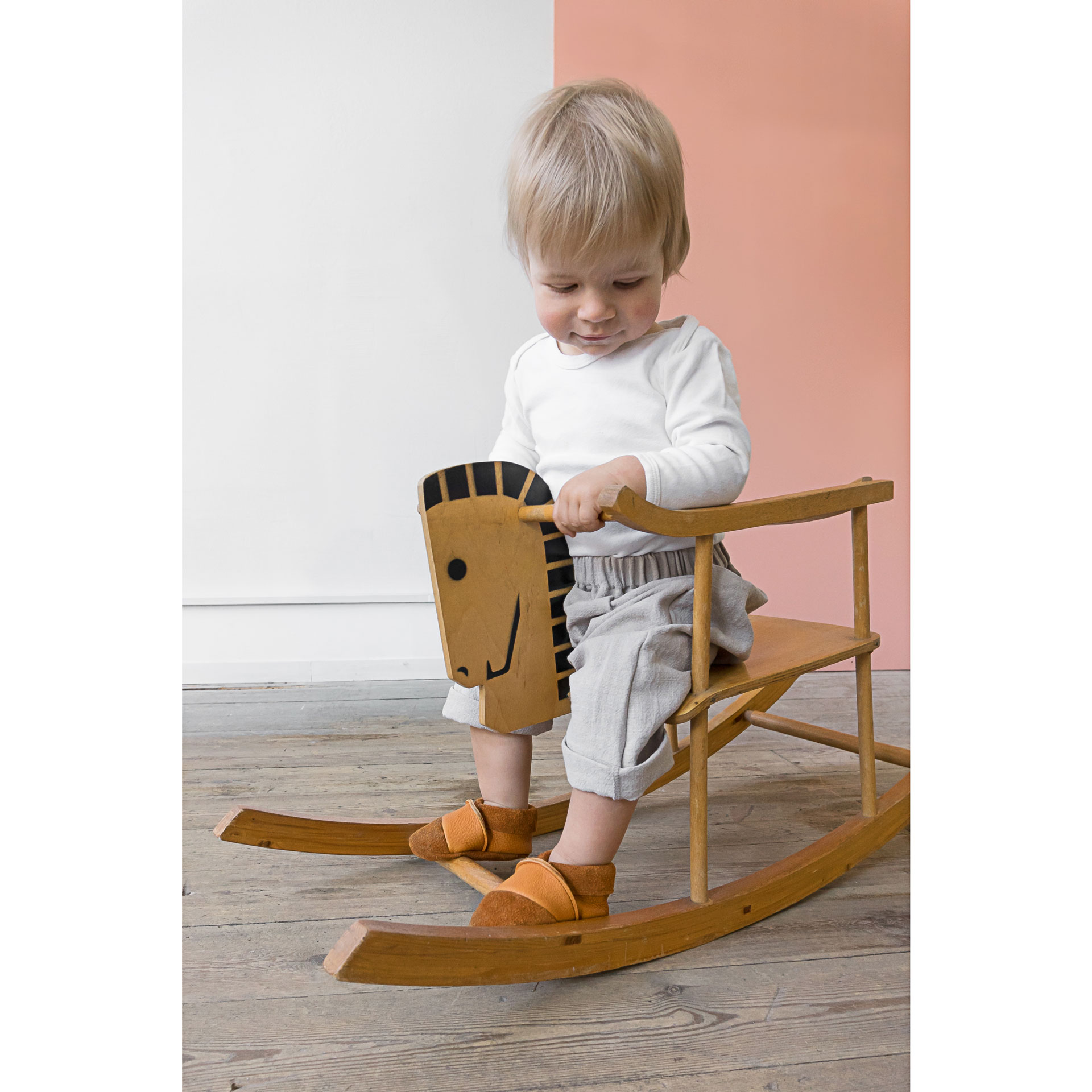 Kind sitzt auf Schaukelpferd und trägt Lauflernschuhe MOQ in Cognac