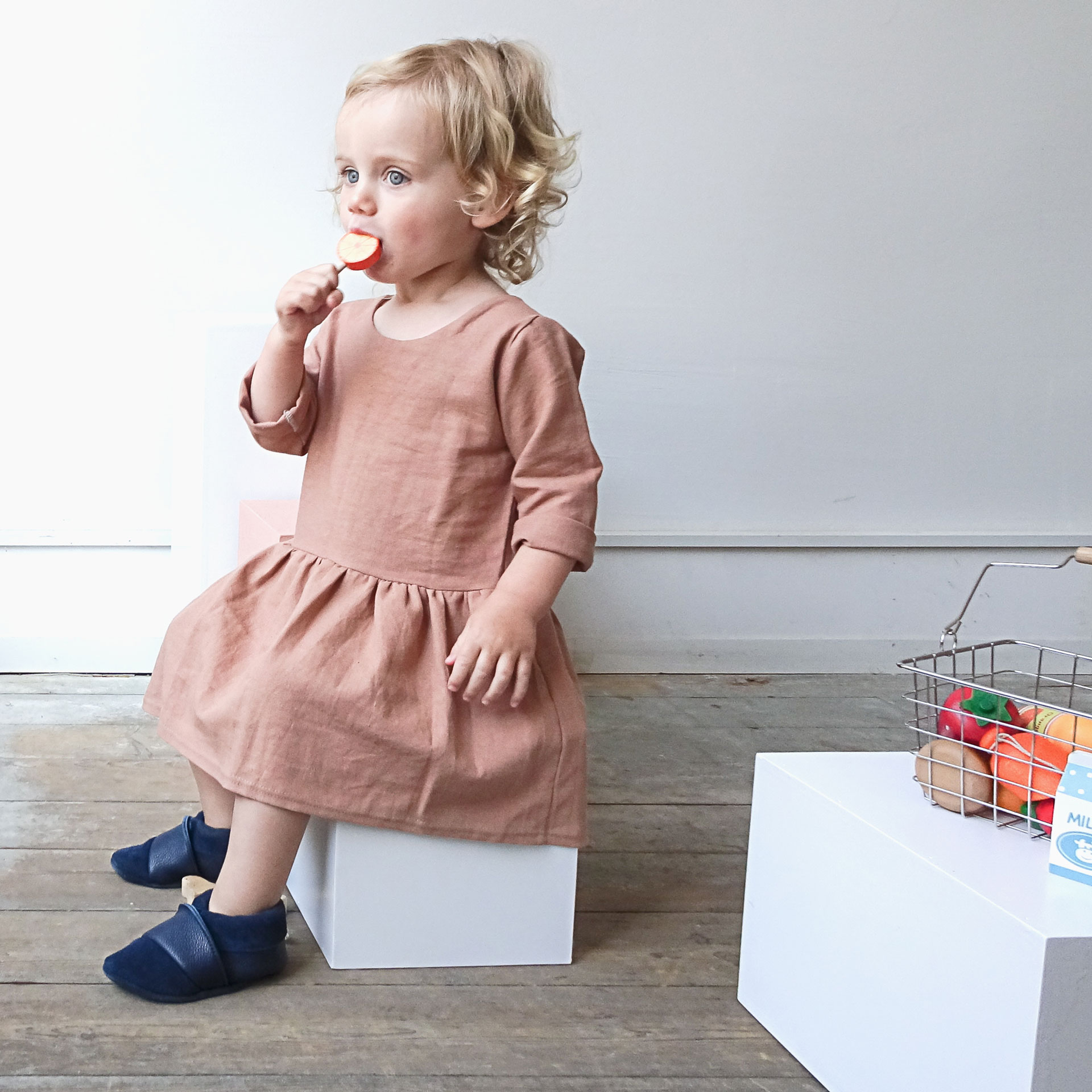 Kind mit Lutscher sitzt auf Block und trägt Lauflernschuhe MOQ in Dunkelblau