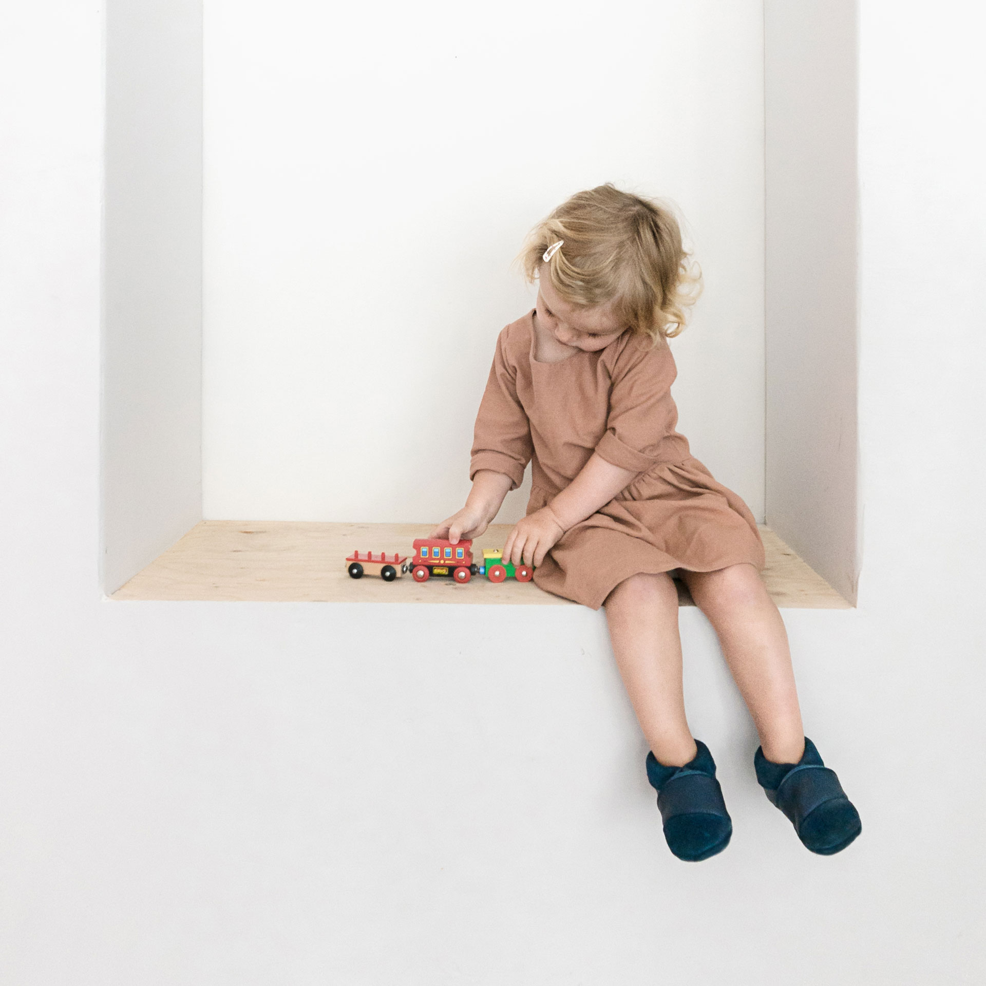 Mädchen spielt mit Holzzug und trägt Lauflernschuhe MOQ aus dunkelblauem Naturleder