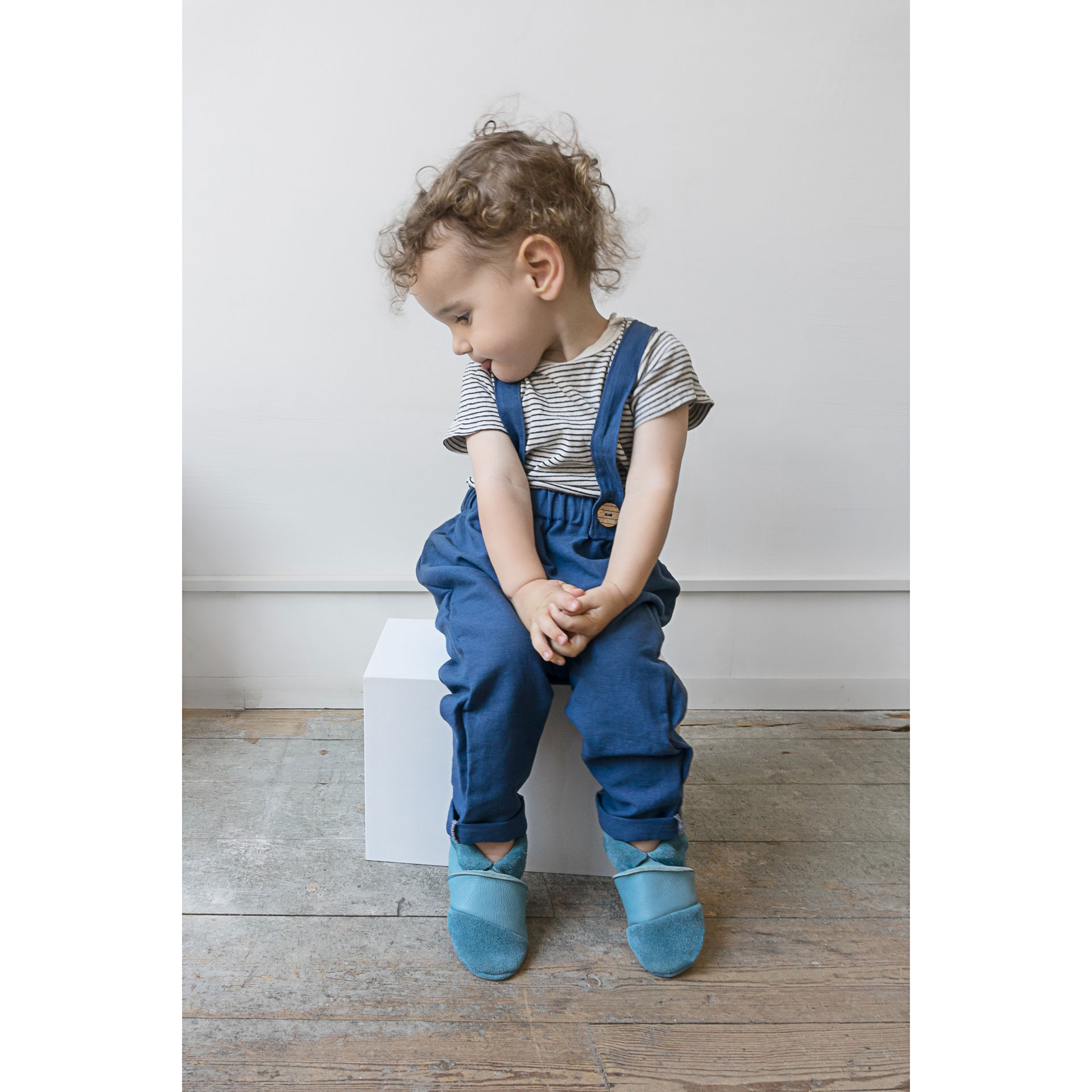 Junge sitzt auf Block und trägt Barfußschuhe für Kinder MOQ in hellblau.