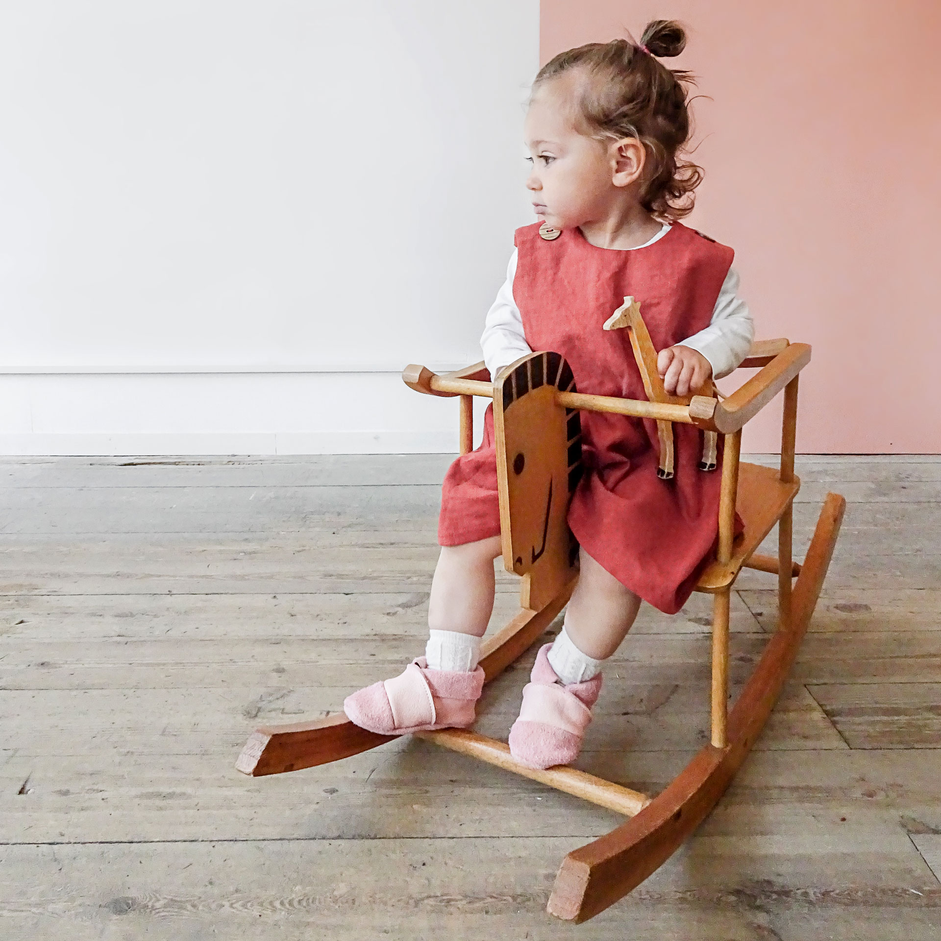 Mädchen mit Holzgiraffe sitzt auf Schaukelpferd und trägt Lauflernschuhe MOQ in rosa