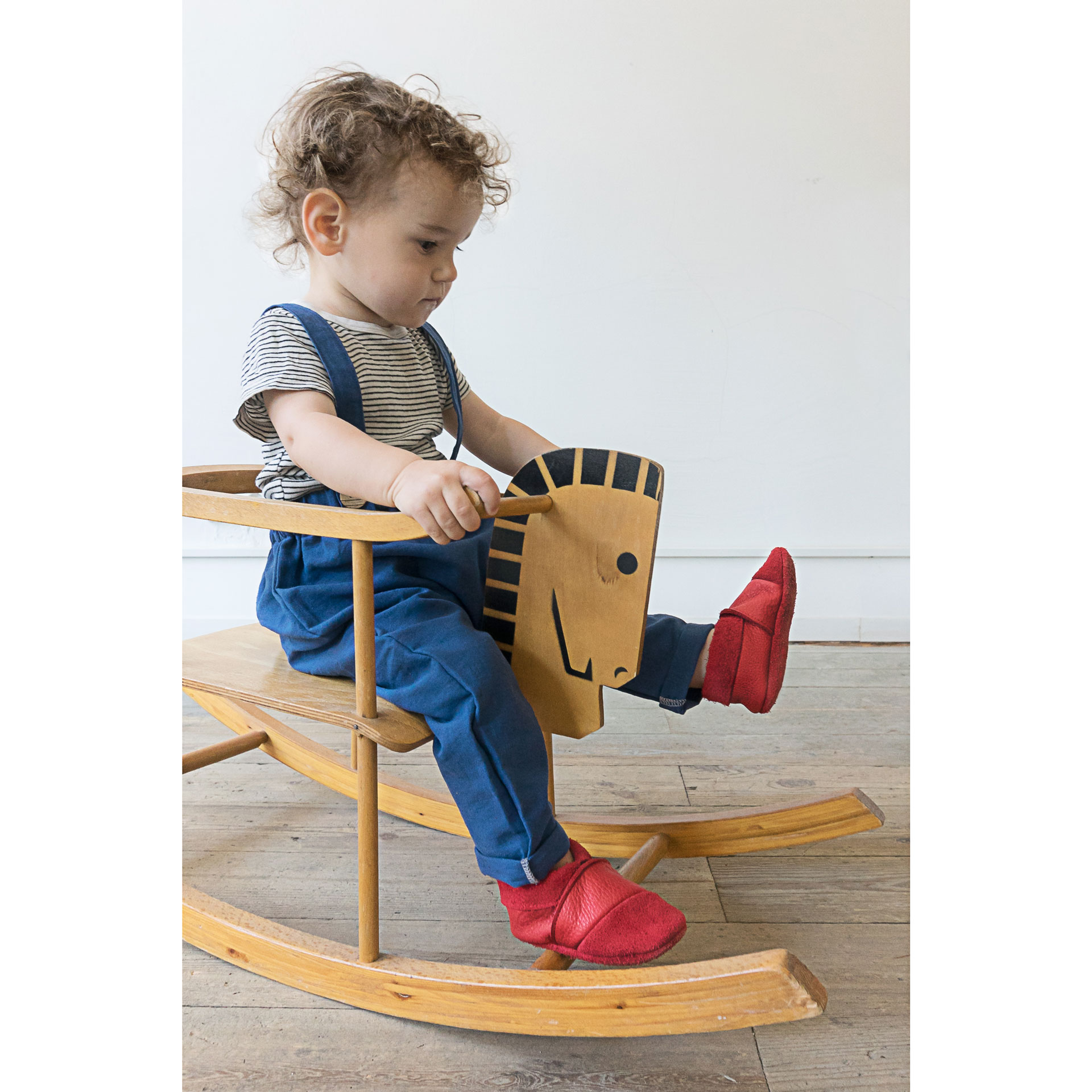 Kind sitzt auf Schaukelpferd und trägt Lauflernschuhe MOQ in Rot