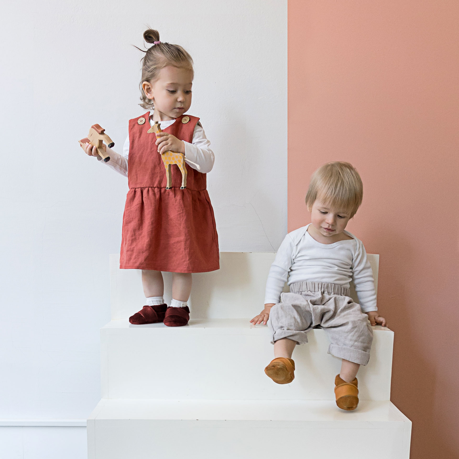 Zwei Kinder tragen Lauflernschuhe MOQ in den Farben Weinrot und Cognac.