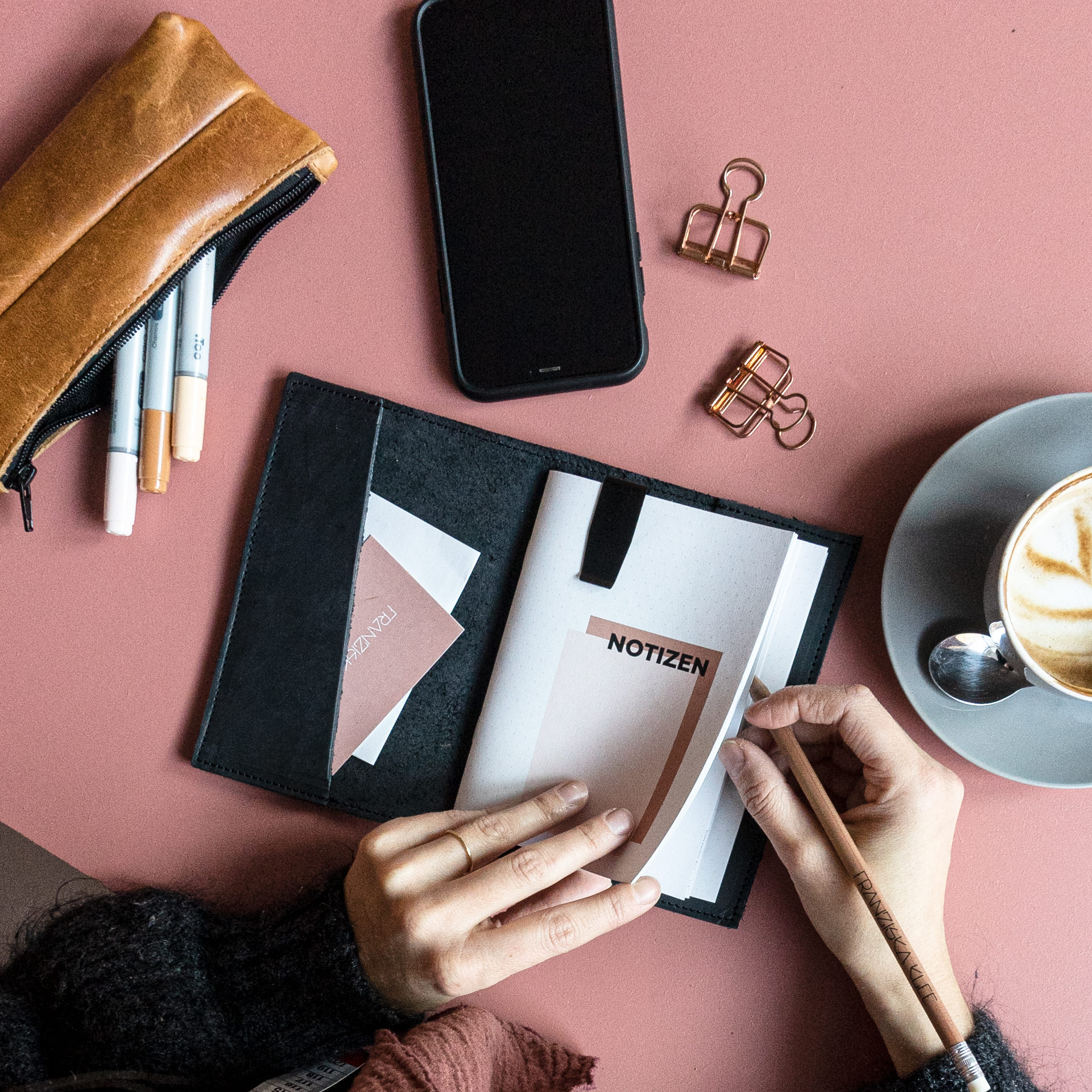Eine Frau sitzt am Tisch und schreibt Notizen in ihre Notizbuchhülle.