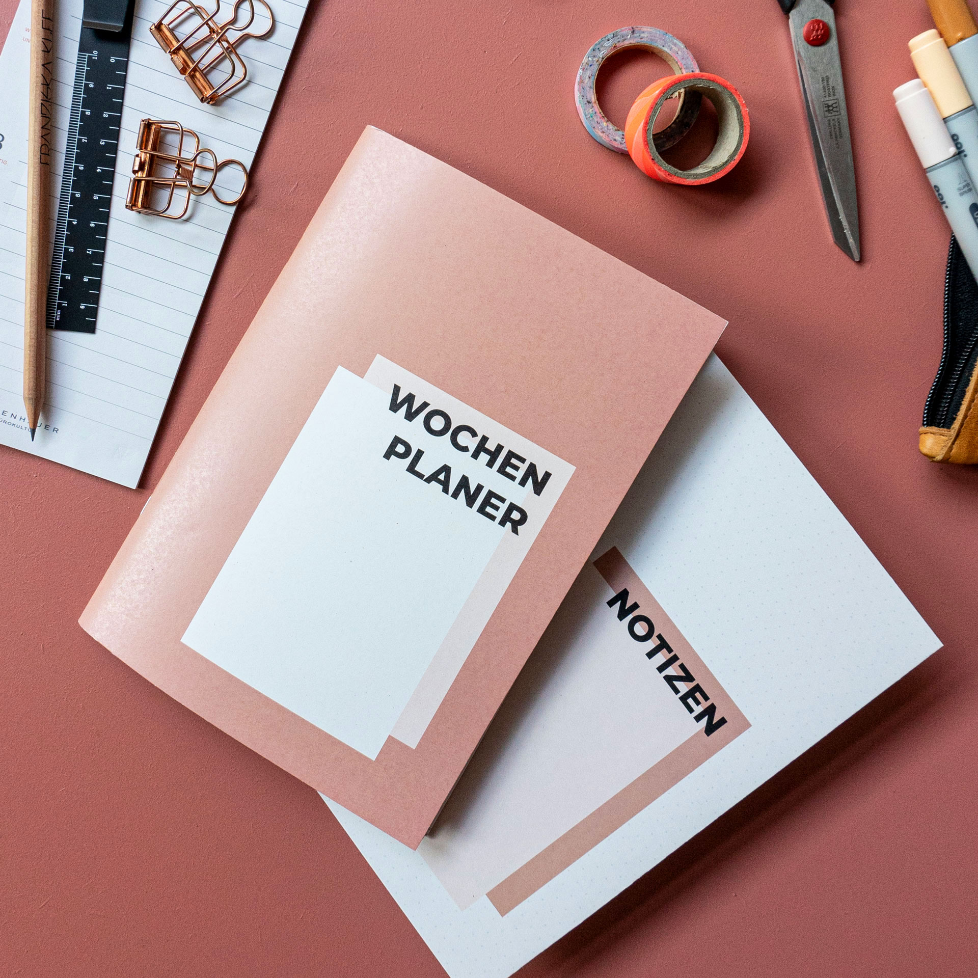 Wochenplaner und Notizheft liegen mit Schreibwaren auf dem Tisch.