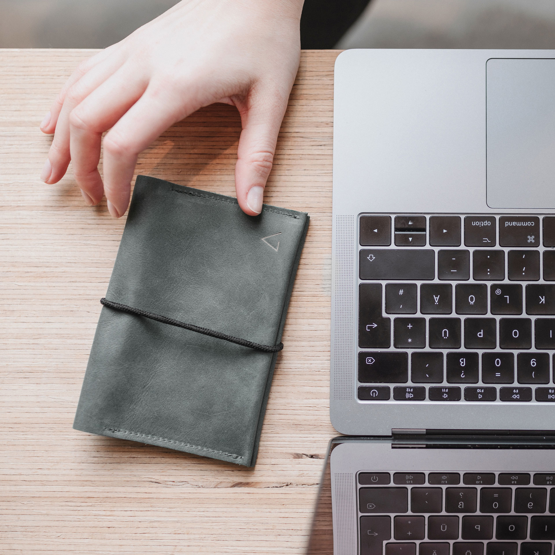 Portemonnaie OLI LARGE in Steingrau mit schwarzem Verschlussband neben Laptop