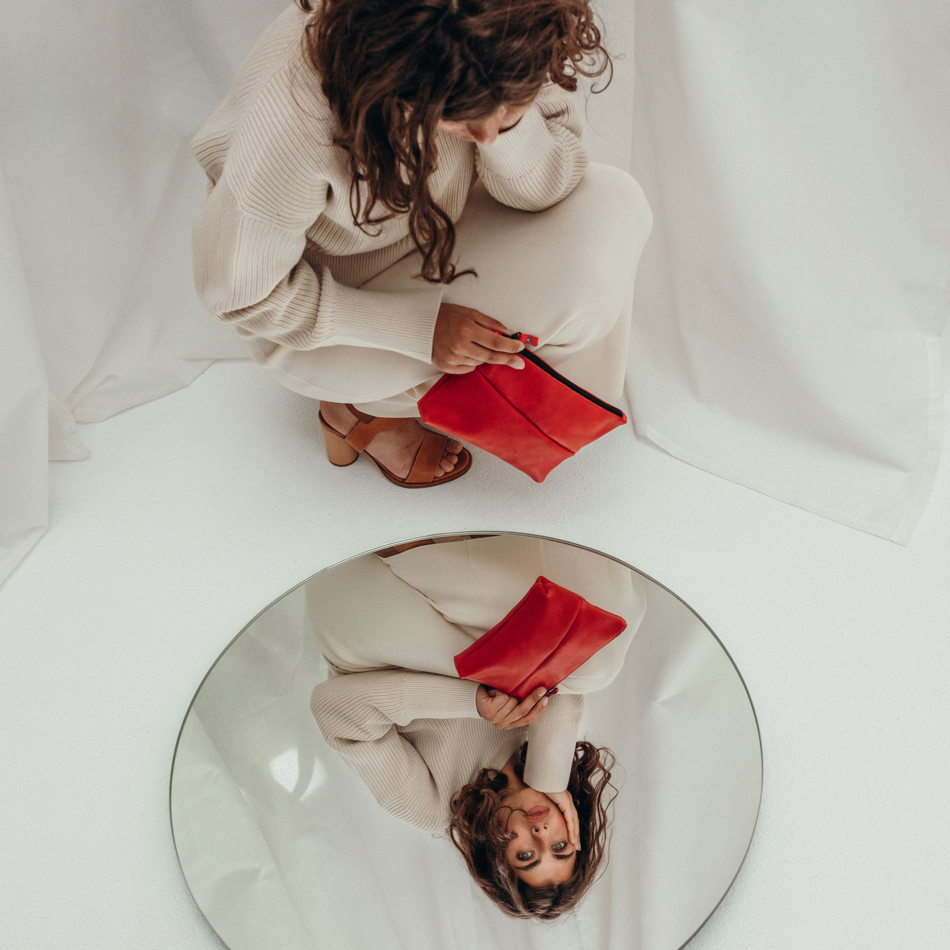 Model hält Pouch FRA in Rot und blickt in Spiegel