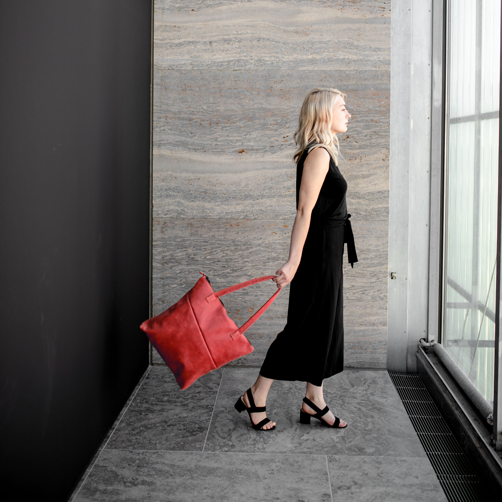 Model steht seitlich da und hält Shopper FIA in der Farbe Rot in der Hand.