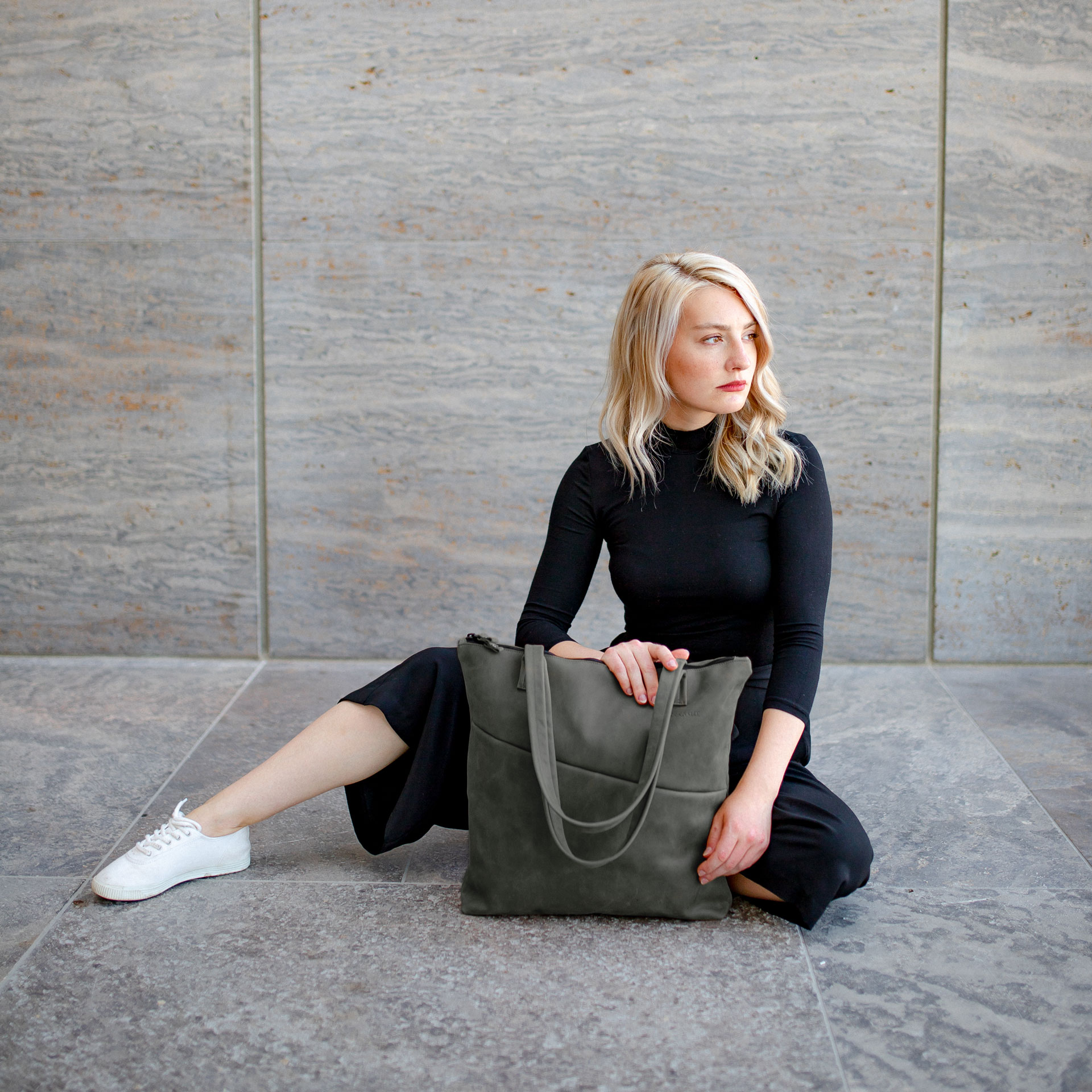 Model sitzt auf dem Boden. Vor ihr steht der Shopper FIA in der Farbe Steingrau.