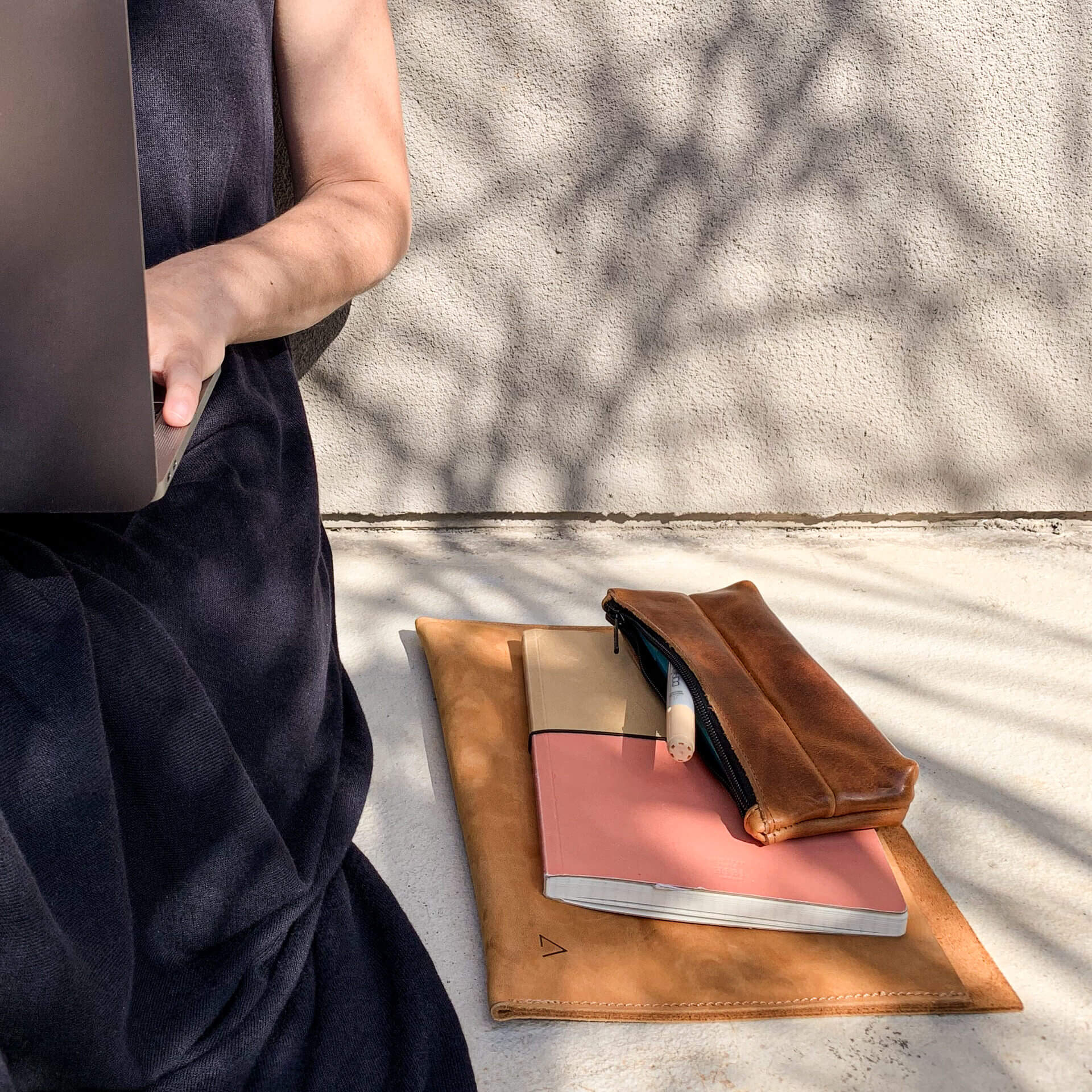 Stifteetui PEN aus nachhaltigem Naturleder in Cognac geölt auf Notizbuch und Laptophülle neben sitzender Frau