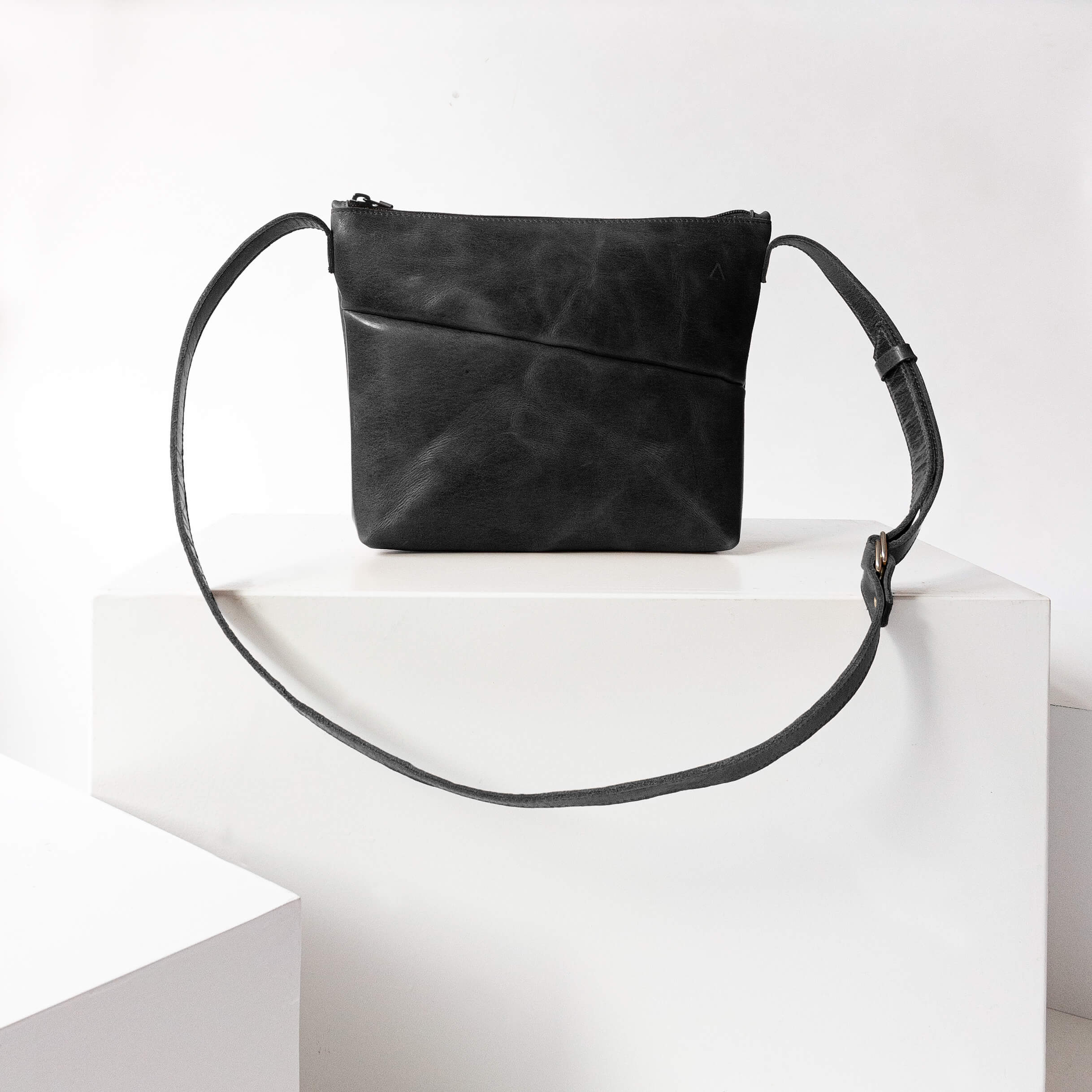Vorderseite der Umhängetasche IDA aus nachhaltigem Naturleder in Schwarz geölt auf Block stehend