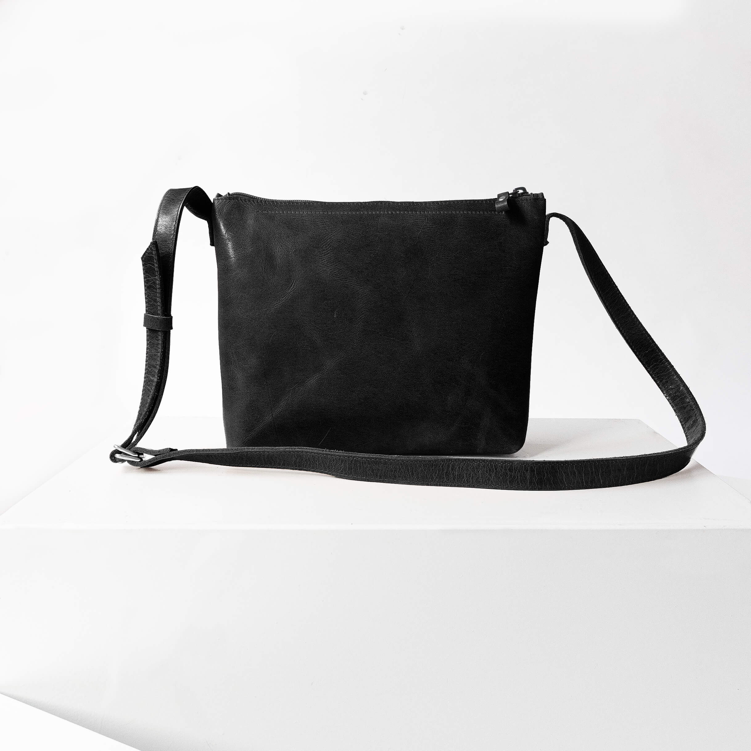 Rückseite der Umhängetasche IDA aus nachhaltigem Naturleder in Schwarz geölt auf Block stehend
