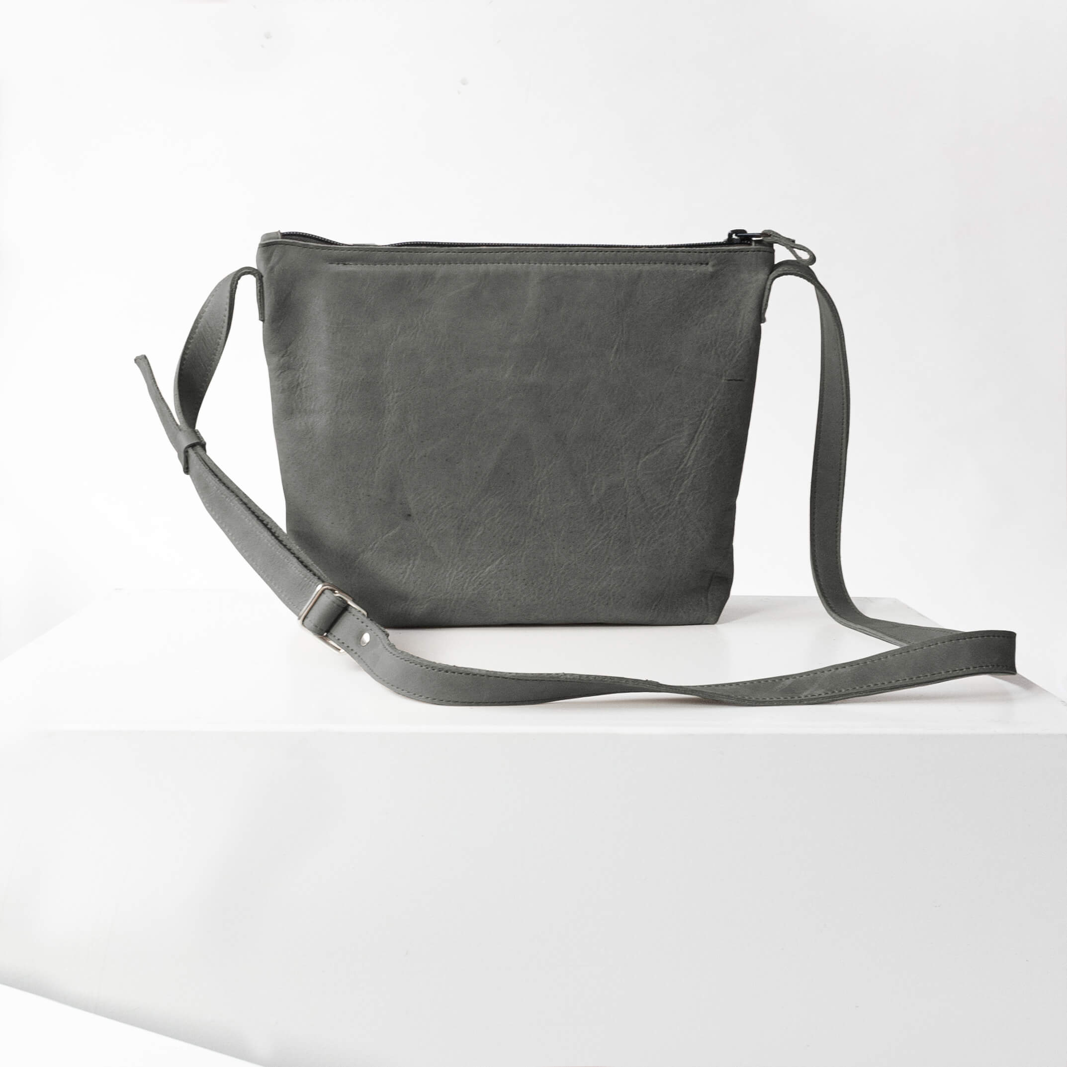 Rückseite der Umhängetasche IDA aus nachhaltigem Naturleder in Steingrau auf Block stehend
