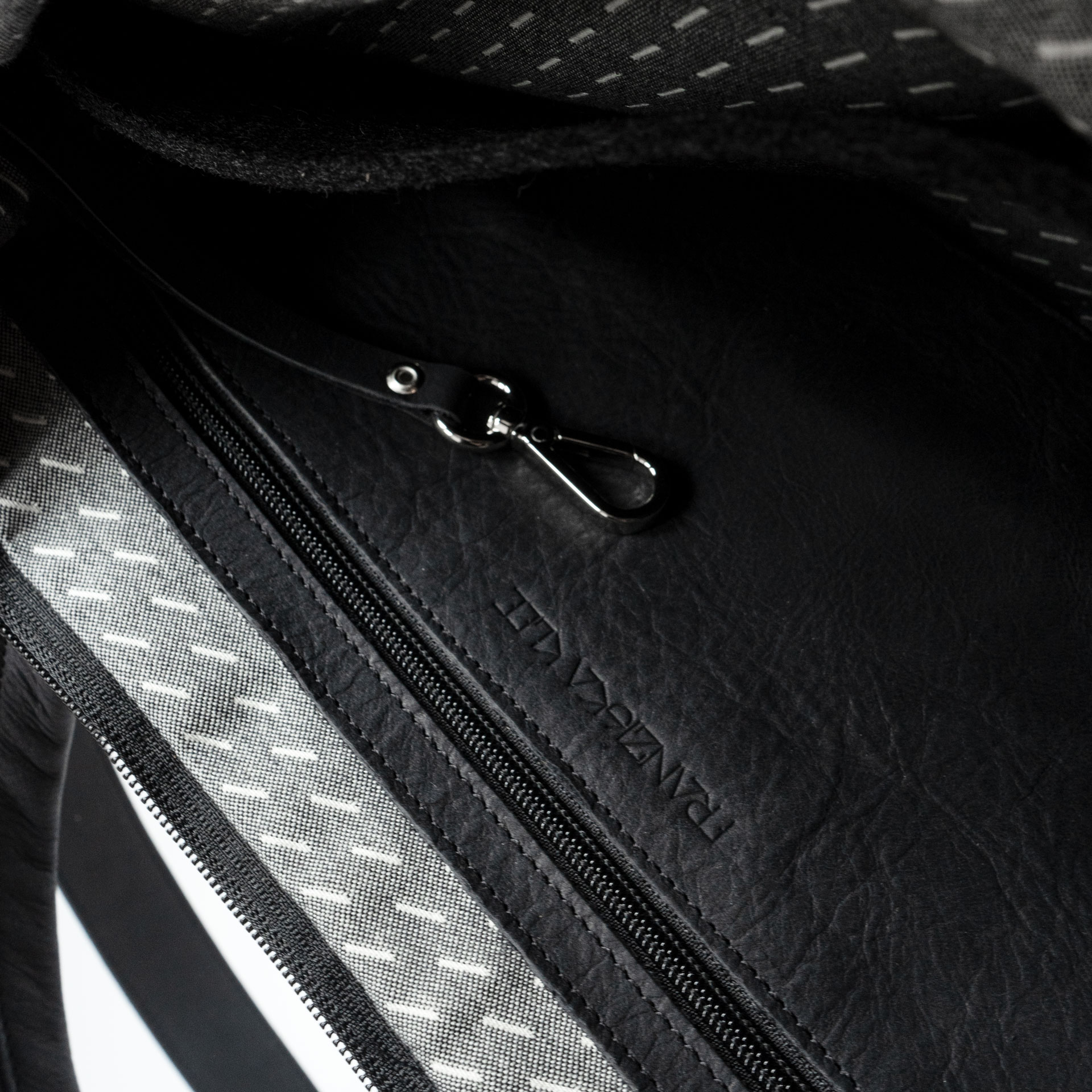 Detailansicht des Innenfachs mit Logoprägung und Schlüsselkarabiner in der Umhängetasche ANA aus Naturleder in Kohle