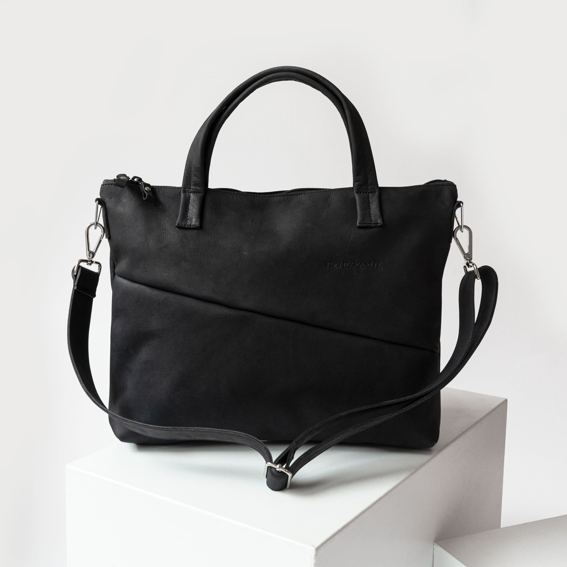 Vorderseite der Umhängetasche ANA aus nachhaltigem Naturleder in Kohle mit verstellbarem Träger und dezenter Logoprägung