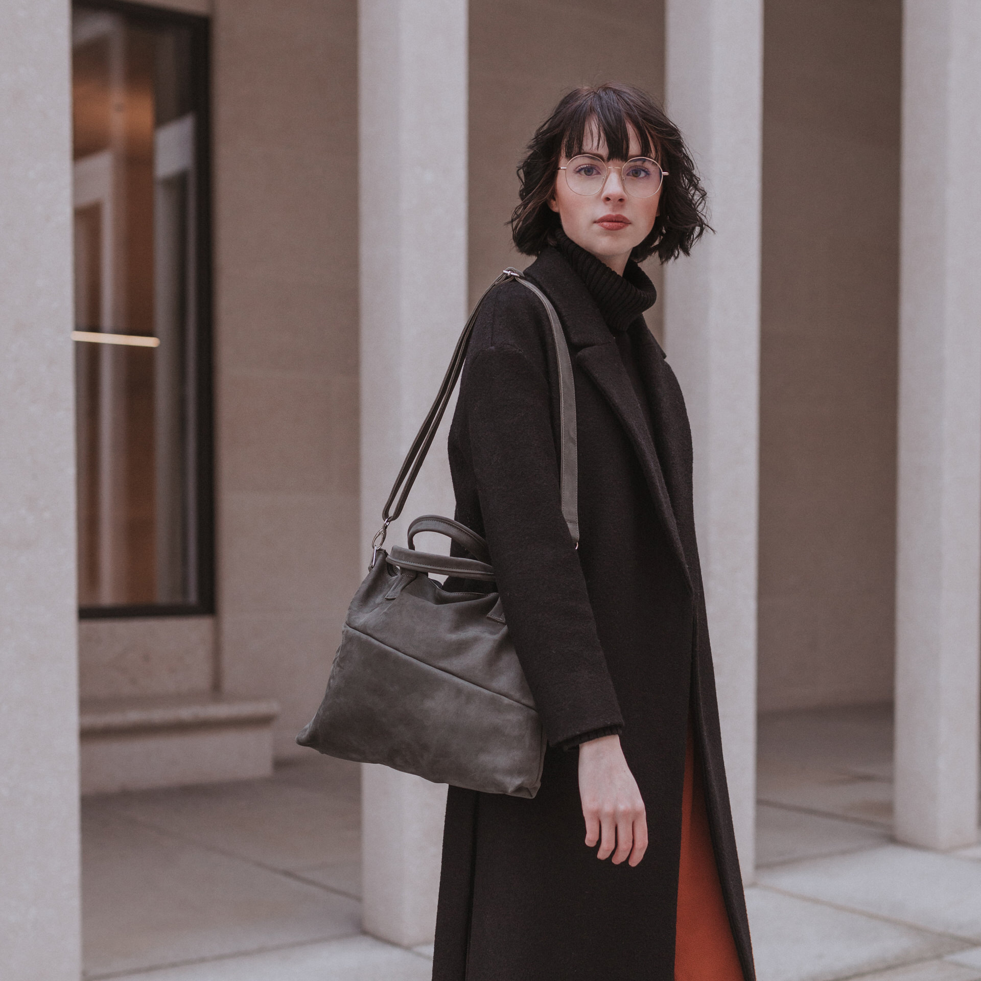 Model mit Handtasche ANA aus steingrauem Naturleder mit Henkeln und Schultergurt