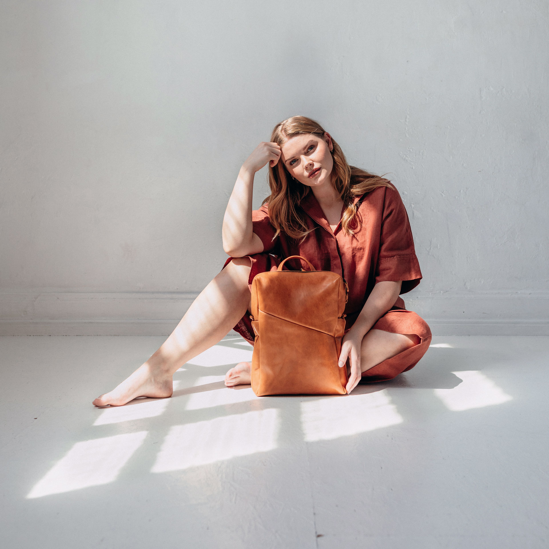 Model sitzt auf dem Boden und hat den Rucksack NEO Small in der Farbe Cognac geölt vor sich stehen.