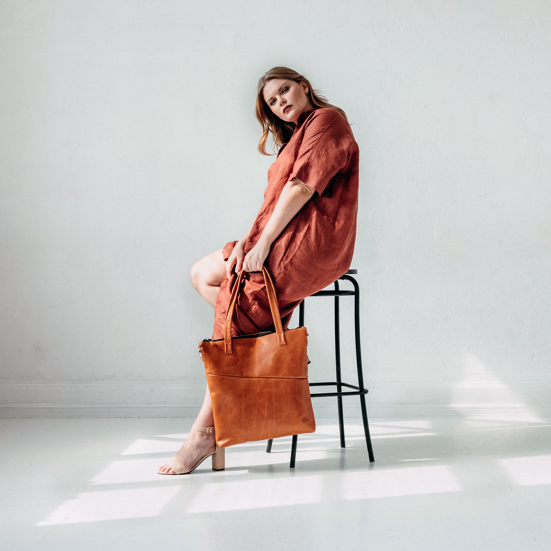 Model sitzt auf einem Hocker und hält Shopper FIA in der Farbe Cognac geölt in der Hand.