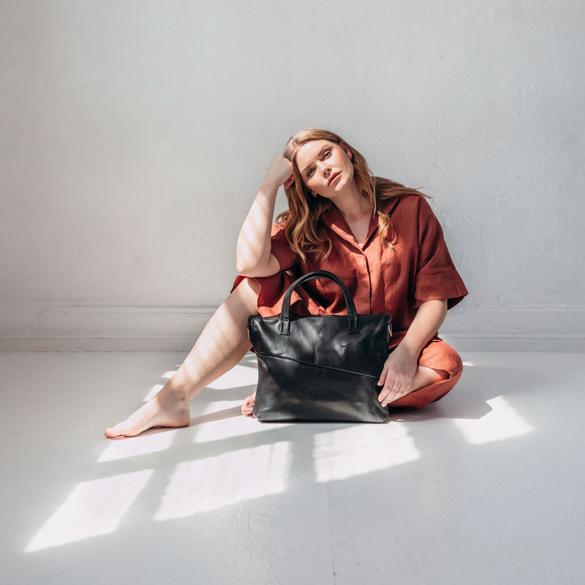 Model sitzt auf dem Boden und hat Umhängetasche ANA in der Farbe Schwarz geölt vor sich stehen.