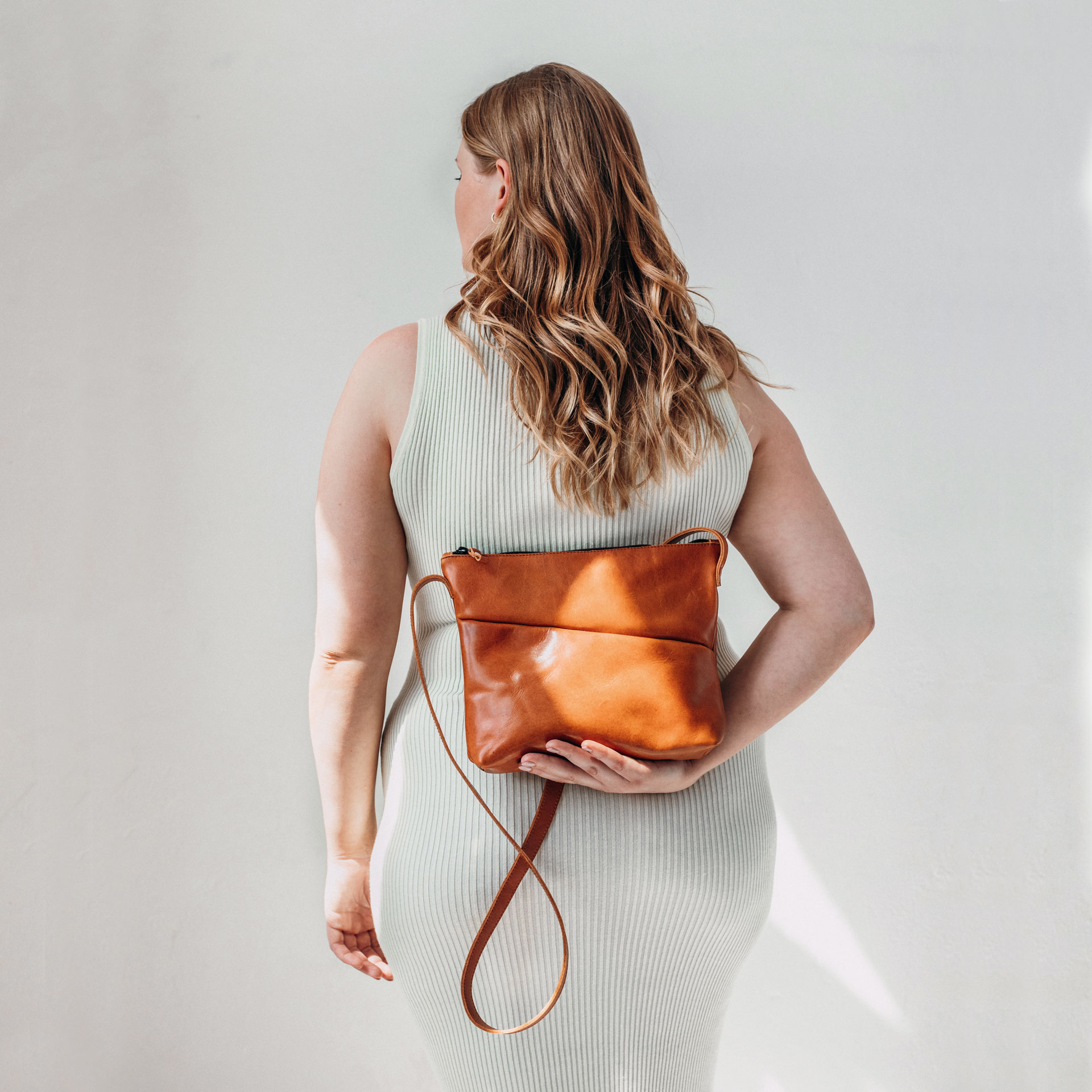 Model hält Umhängetasche IDA in der Farbe Cognac geölt hinter dem Rücken in der Hand.