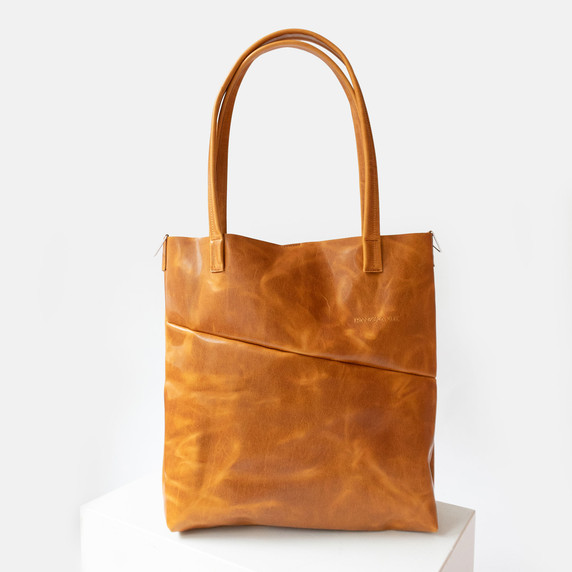 Vorderseite der Wickeltasche MIA MIDI aus nachhaltigem Naturleder in Cognac geölt mit langen Henkeln, Halterung für Umhängegurt und dezenter Logoprägung