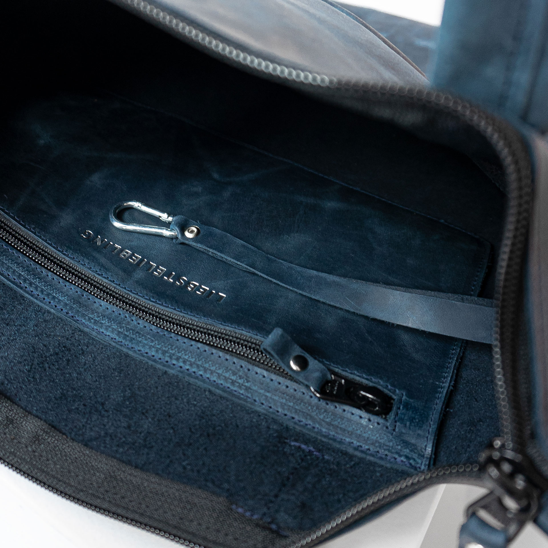 Detailansicht innen der Wickeltasche MIA MIDI aus Naturleder in Dunkelblau mit Reißverschlussinnenfach, Schlüsselkarabiner und individuelle Prägung in Silber