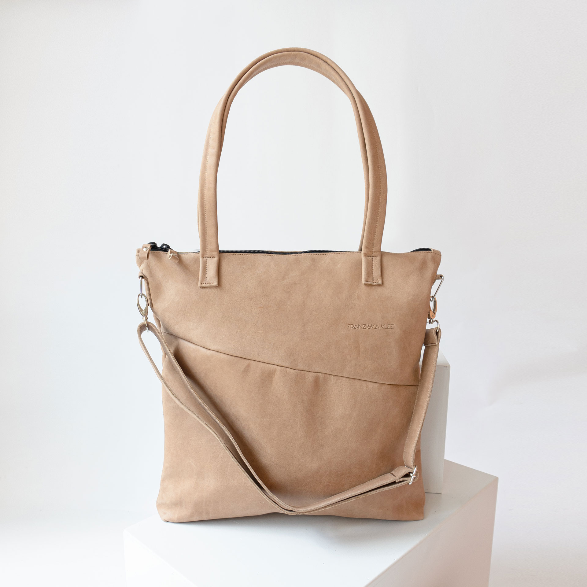 Vorderseite der Wickeltasche MIA MIDI aus nachhaltigem Naturleder in Hellbraun mit langen Henkeln, abnehmbarem Umhängegurt und dezenter Logoprägung