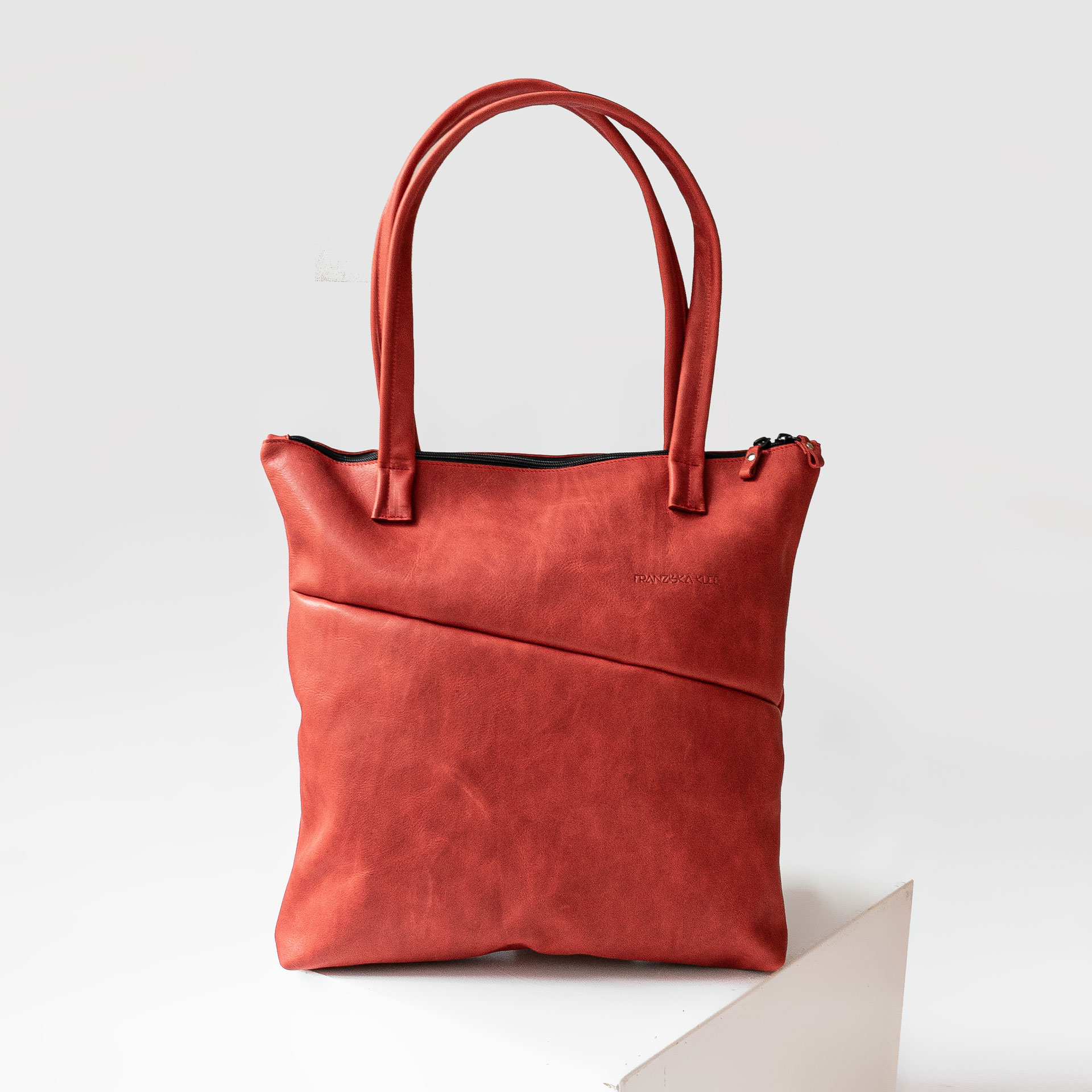 Vorderseite der Wickeltasche MIA MIDI aus nachhaltigem Naturleder in Rot mit langen Henkeln und dezenter Logoprägung