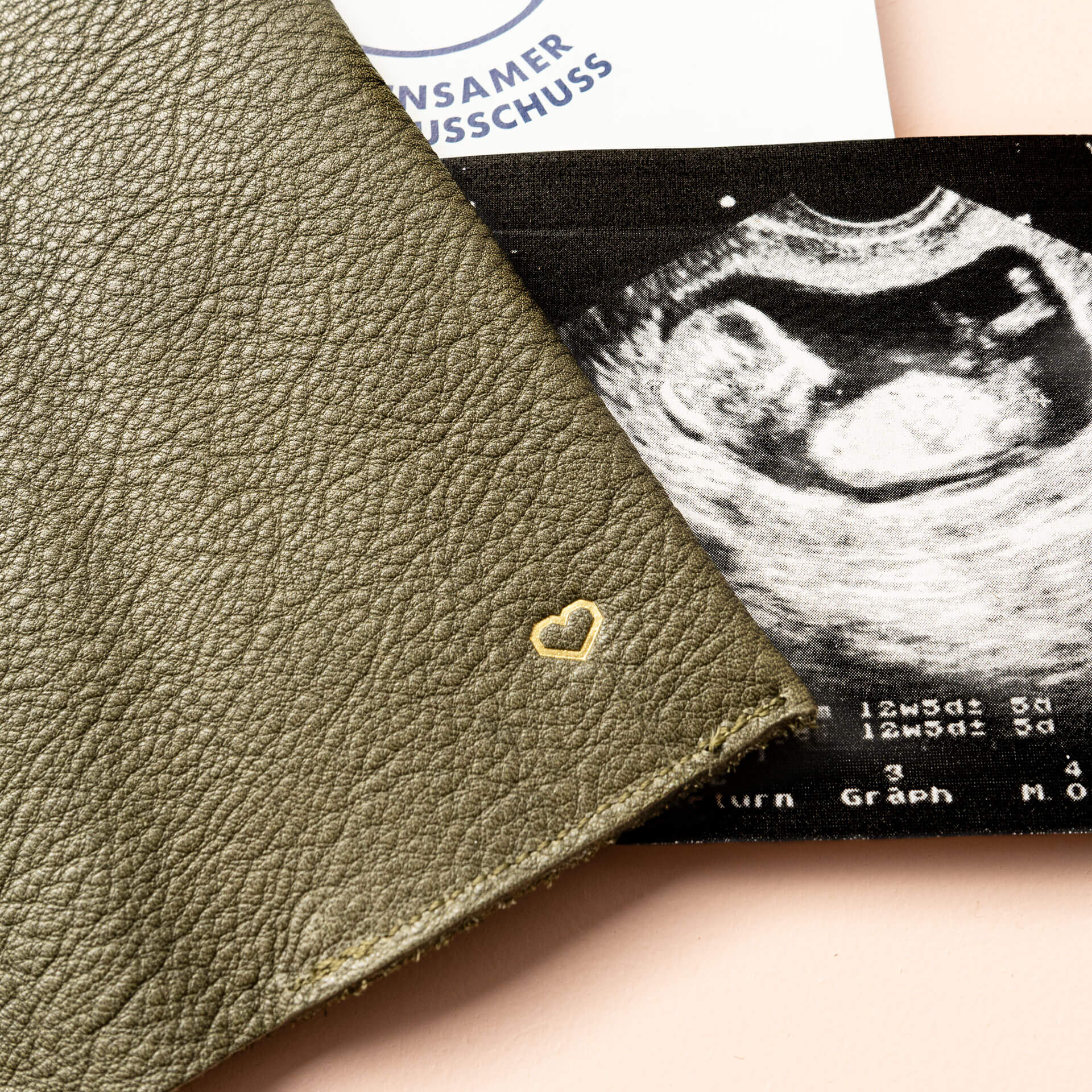 Mood Shot Detailansicht einer Herzprägung in Gold auf Mutterpasshülle EVE in Oliv