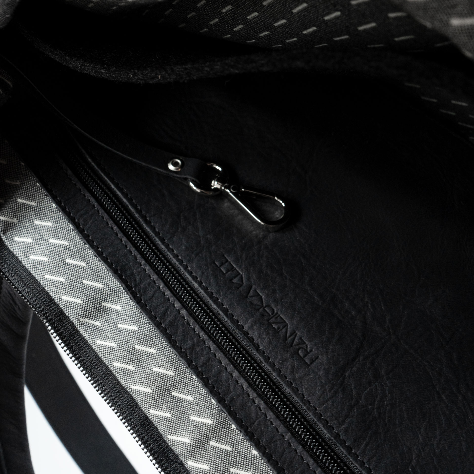 Detailansicht des Innenfachs mit schlichter Logoprägung und Schlüsselkarabiner in der Umhängetasche ANA aus Naturleder in Schwarz geölt