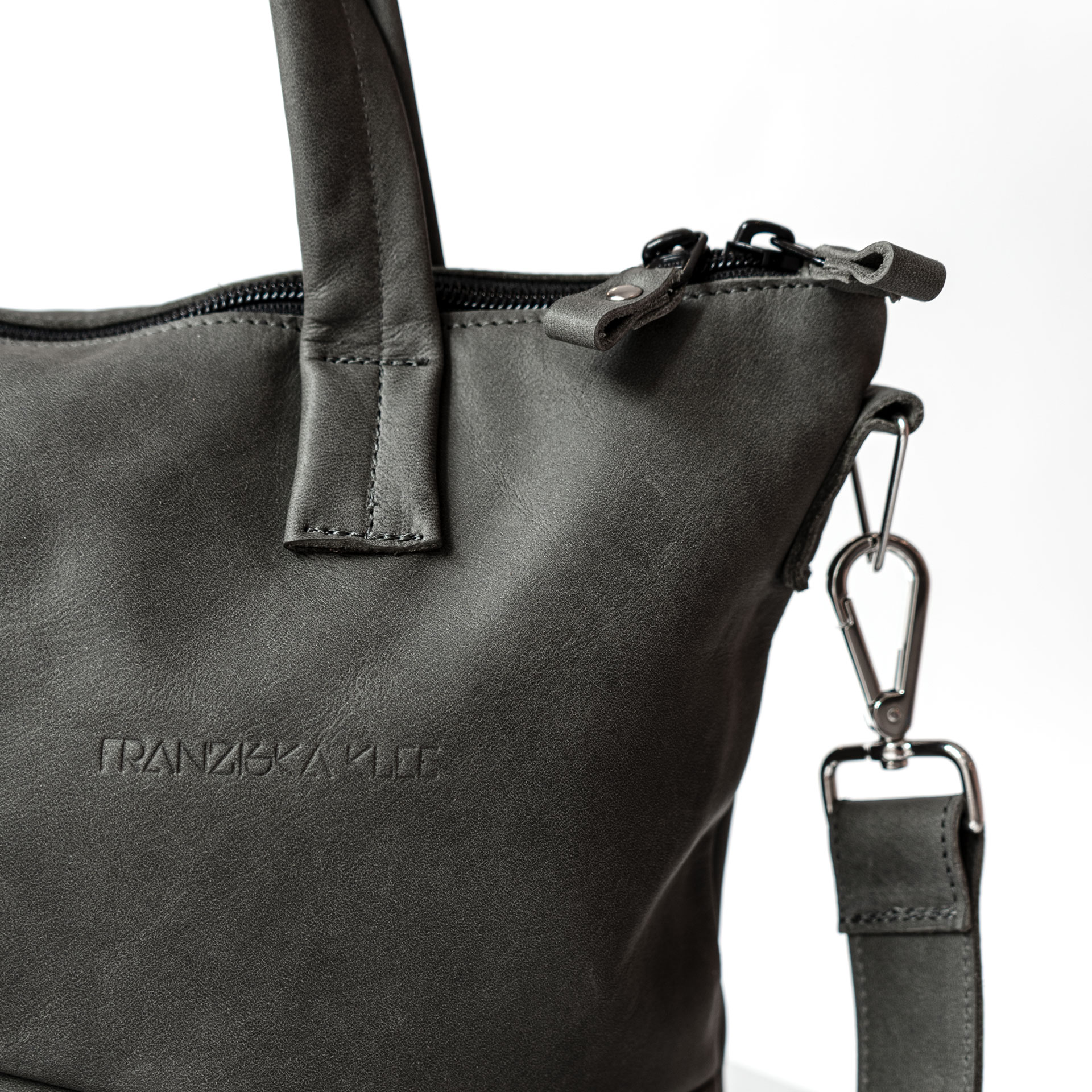 Detailansicht der Trägeraufhängung und Henkelnaht an Umhängetasche ANA aus nachhaltigem Naturleder in Steingrau mit schlichter Logoprägung